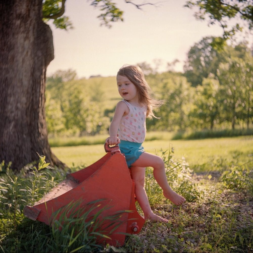Girl seated on a bucket under a tree, medium format film